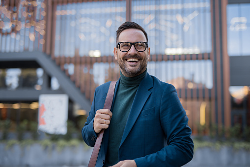 Person in blue blazer and green turtleneck standing in front of a modern building with wooden slats.